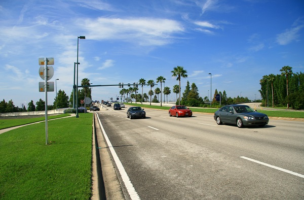 Wide view of a Florida highway lined with palm trees, showing cars driving under a clear, sunny sky.