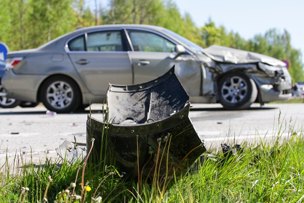 Damaged car on the side of the road after a hit-and-run crash, with broken debris in the grass. (Adobe - 422912837)