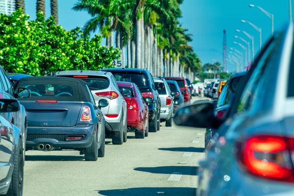 A view of heavy traffic on a palm tree-lined street in West Palm Beach, Florida, with cars densely packed on the road under a clear blue sky.